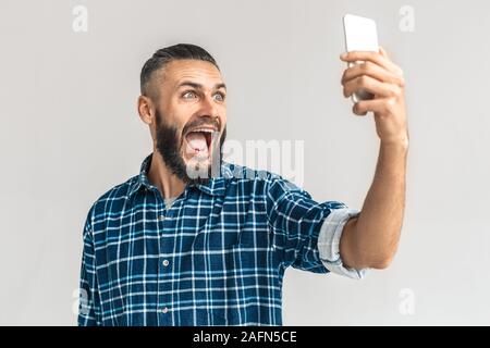 Freestyle. Kerl in kariertem Hemd stehen isoliert auf weißem Video-chats auf dem Smartphone Lächeln aufgeregt Stockfoto