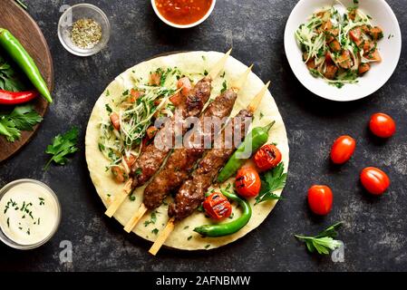 Türkische Adana Kebab mit frischem Gemüse auf fladenbrot über schwarzen Stein. Lecker essen im arabischen Stil. Ansicht von oben, flach Stockfoto