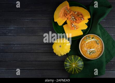 Kürbis creme Suppe in einer Schüssel auf einem dunklen Hintergrund mit grünen, kürbisscheiben. Flach. kopieren. Stockfoto