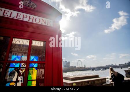 Berühmte rote Telefon Zelle in der Sonne an der Themse in London. Stockfoto