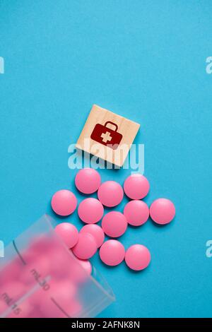 Medizinische Zeichen auf einem holzwürfel Neben rosa Tabletten aus einem Plastikbecher auf blauem Hintergrund. Ansicht von oben. Vertikale. Stockfoto