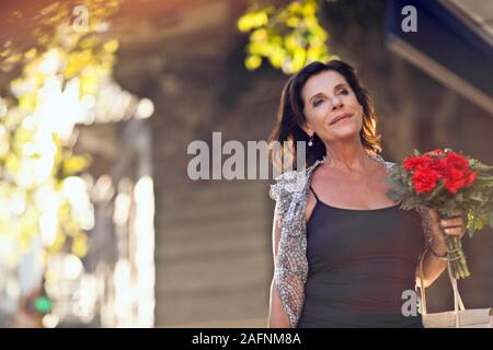 Reife Frau auf dem Bürgersteig, mit Blumen. Stockfoto