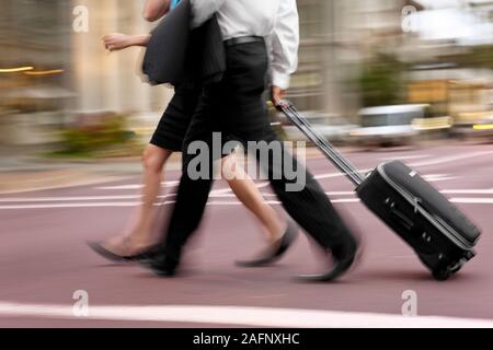 Zwei Kollegen das Überqueren einer Straße der Stadt ziehen ein Koffer. Stockfoto