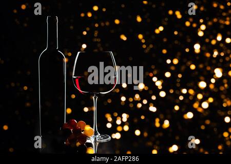 Elegante Rotwein Glas, Flasche Wein und Trauben auf dem dunklen Hintergrund und verschwommenes defokussierten Lichter als Weihnachtsschmuck Hintergrund. Party Konzept. Valentinstag, Geburtstag Konzept. Stockfoto