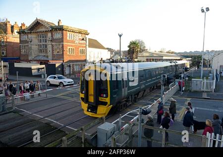 Fußgänger und ein Auto warten als Multiple Unit Train kreuzt den Bahnübergang in Paignton Station an der englischen Riviera in Devon Stockfoto