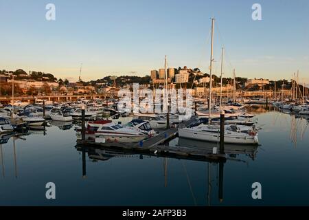 Jachten und andere Yachten in der Marina bei Torquay, Devon, UK festgemacht, wie die Sonne, die Stadt hinter die Beleuchtung mit Orange. Stockfoto