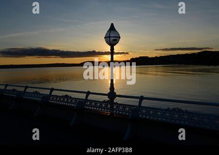 Die Sonne geht hinter einem lichtmast auf Prinzessin Pier in Torquay, Devon Mitte November. Stockfoto