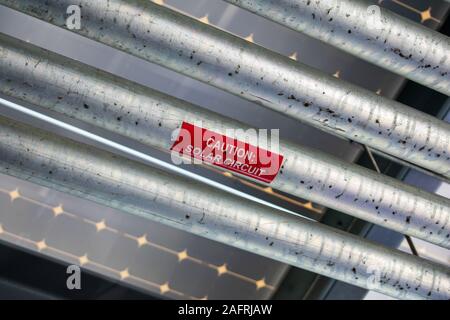 Vorsicht Solarkreis rote Aufkleber auf schmutzige metallene Oberfläche der Solarkreislauf unter einem Solarzellen als Vordach auf der Oberseite des Parkhauses installiert Stockfoto