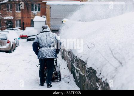 Ein Mann räumt auf dem Hof entfernt die Schneefräse Stockfoto