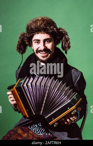 Positiver Mann mit Akkordeon posiert im Studio Stockfoto