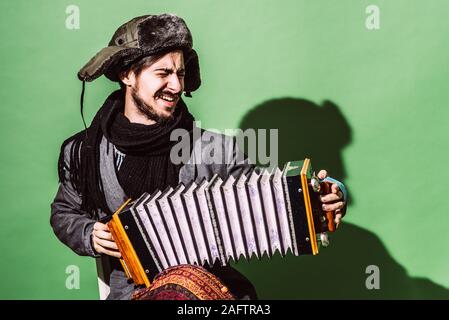 Positiver Mann mit Akkordeon posiert im Studio Stockfoto