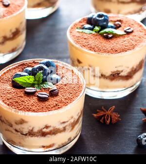 Dessert Tiramisu in Gläsern, mit Heidelbeeren und Minze mit Kaffeebohnen dekoriert, das Konzept der köstlichen Leben Stockfoto