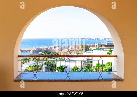 Terrasse mit Bogen mit Blick auf das Meer. Eine halbrunde Fenster mit Blick auf die Villa und tropischen Bäumen. Meerblick von einem Luxus Resort. Stockfoto