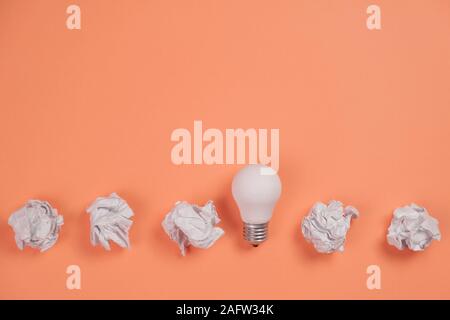 Kreativität, Inspiration, gute Geschäftsidee Konzept mit weißem Licht Lampe und Papier Kugel auf orangefarbenem Hintergrund zerknittert. Flach, Ansicht von oben, kopieren Raum Stockfoto
