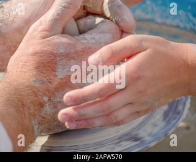 Erwachsene und Kinder Hände über das Rad des Töpfers. Das Kind lernt, ein Produkt aus Ton zu machen Stockfoto