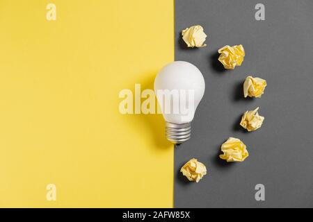 Neue Idee Konzept mit zerknitterten Office Papier und Weiße Glühbirne auf schwarzem und gelbem Hintergrund. kreative Lösung beim Brainstorming Sitzung. Flach Stockfoto