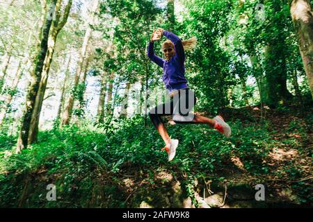 Portrait sorglos weiblichen Personal trainer Wandern, Springen in Wald Stockfoto