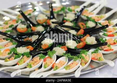 Salat Snacks in Keramik schwarz und weiß Löffel an der Stand-up-Party oder Buffet Lunch. Leckere Gerichte mit frischem Gemüse auf großen runden Metall oder Silber Teller auf dem Tisch. Catering Service Stockfoto
