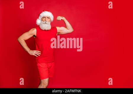 Porträt von Ernst santa claus in hat seine Trizeps angezeigt in der Ausbildung tragen Sportswear Kappe über den roten Hintergrund isoliert Stockfoto