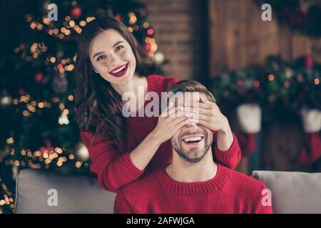 Guess Who. Foto von charmanten Paar schließen Augen verbringen Heiligabend im eingerichteten Girlande lichter Zimmer sitzen in der Nähe von neujahr Baum auf gemütlichen Sofa Stockfoto