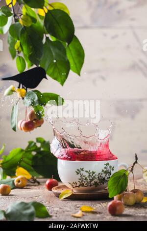 Splash in einem Porzellan Tasse roter Tee. Tee Zeremonie. Lackiert in China. In einem Raum mit grünem Laub eingerichtet Stockfoto