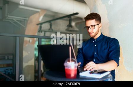 Junge attraktive Hipster freelancer Arbeiten von einem Remotestandort aus auf Laptop im Loft Café. Unternehmer im Internet surfen im Coffeshop. Blogger Beiträge zu Social Media Stockfoto