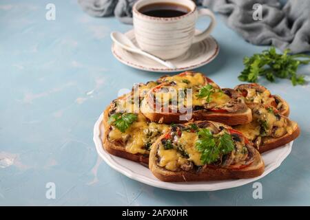 Warme Sandwiches mit Tomaten, Pilzen und Käse auf einem hellblauen Hintergrund mit einer Tasse Kaffee, Kopie Raum Stockfoto