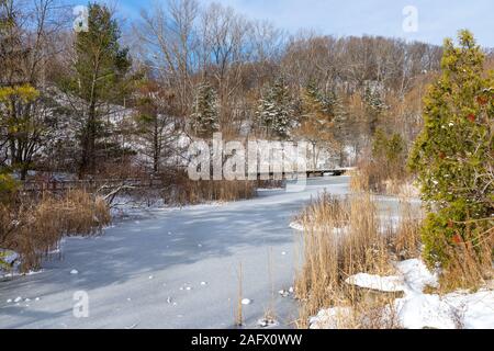 Gefrorener Fluss in einem Feld umgeben von trockenem Grün und Holzzäune unter blauem Himmel Stockfoto