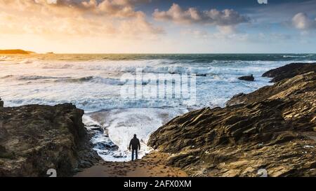 Einen Panoramablick auf ein Mann stand am Strand und beobachten die ankommenden Wellen in eine stürmische See an wenig Fistral in Newquay in Cornwall. Stockfoto