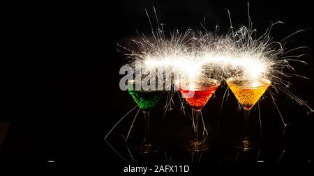 Realistische Aufnahme von drei bunten Cocktails mit Funkenlicht an Schwarzer Hintergrund Stockfoto