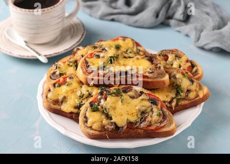 Warme Sandwiches mit Tomaten, Pilzen und Käse auf einem hellblauen Hintergrund mit einer Tasse Kaffee, horizontale Ausrichtung Stockfoto