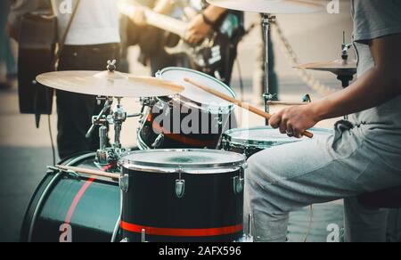 Ein Schlagzeuger in grau Sportswear spielt Holzstäbchen auf ein Drum Kit, Einstellung der Rhythmus mit einer Street Band der Musiker von der Sonne beleuchtet. Stockfoto
