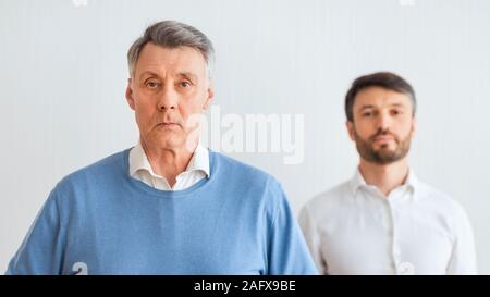 Ernsthafte älterer Mann und Middle-Aged Sohn gegen Weiße Wand Stockfoto