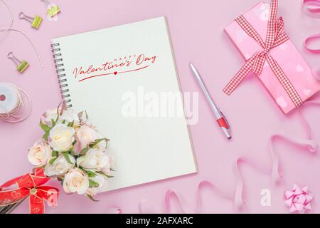 Mockup Notebook auf rosa Hintergrund mit roten Happy Valentines Day, Rosen, Blumenstrauß, Geschenkbox, praktische Fertigkeit und Stift. Mock up für elegantes Design mit Platz Stockfoto