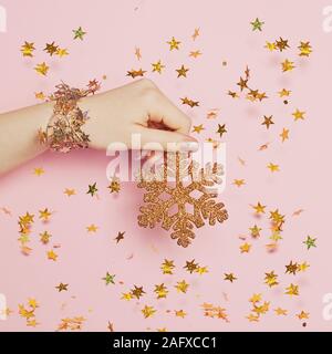 Weihnachtsdekoration Hintergrund. Gold Weihnachten Dekoration Schneeflocke in der Hand auf rosa Hintergrund mit Gold blowing Konfetti Sterne Stockfoto