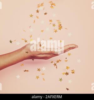 Magische gold Konfetti Sterne Dekoration in weiblicher Hand auf Pastell rosa Hintergrund Stockfoto
