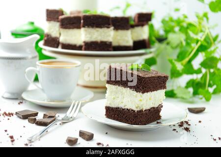 Milch Schokolade Kuchen und Kaffee auf einer Untertasse im Hintergrund mehr Kuchen und einer Anlage Stockfoto
