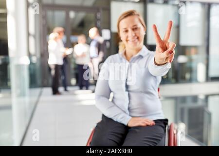 Erfolgreiche junge geschäftsfrau im Rollstuhl macht Sieg Zeichen von Hand Stockfoto