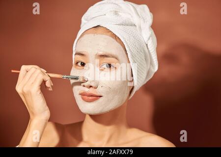 Glückliche Frau mit einem Handtuch auf dem Kopf eine reinigende Maske im Gesicht anwenden Stockfoto