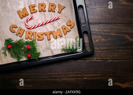 Wörter Frohe Weihnachten aus Cookies auf backblech Holztisch und Dekorationen Stockfoto