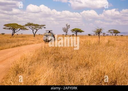 Safari Touristen auf Pirschfahrt mit Jeep Auto im Serengeti National Park in einer schönen Landschaft, Tansania, Afrika Stockfoto