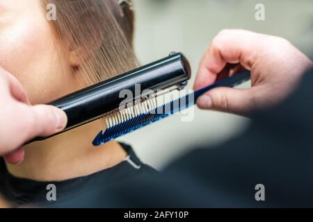 Friseur Hände begradigen braune Haare mit Fön Bügeleisen, hautnah. Stockfoto