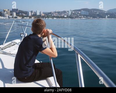 Der Junge sitzt im Bug des Bootes und schaut auf das Meer Stockfoto