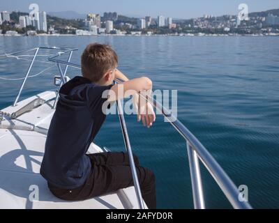 Der Junge sitzt im Bug des Bootes und schaut auf das Meer Stockfoto