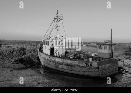 Ein altes Fischerboot auf dem Schlamm bei Ebbe in Schwarz-Weiß bei Brancaster staith, Norfolk, Großbritannien gesehen. Genommen 3. Dez 2019. Stockfoto