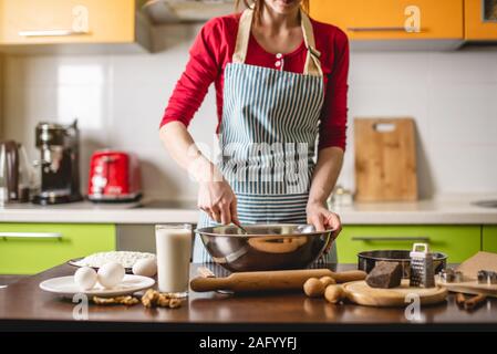 Cook Hausfrau cookies zu Hause auf eine bunte Küche. Eine Frau rührt den Teig in einer Metallschüssel an einem Tisch mit Zutaten Stockfoto