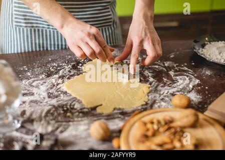 Cook Hausfrau die Weihnachtsplätzchen zu Hause auf eine bunte Küche. Weibliche Hände, Teig die Form der Weihnachtsbäume für den Urlaub Tabelle Stockfoto