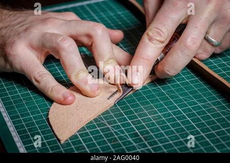 Ein Handwerker in seiner Lederwerkstatt nimmt die Fase ab Stockfoto