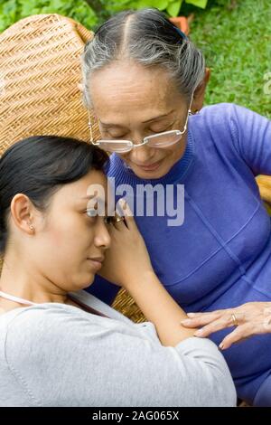 Südostasiatische Familie: Tochter traurig und lehnen Sie ihren Kopf auf die Schulter ihrer betagten Mutter, die versucht, sie aufzumuntern. Stockfoto