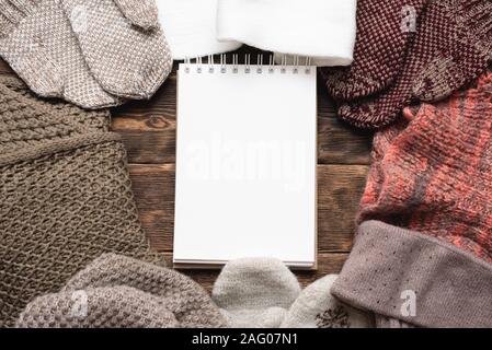 Leere Notepad und Winterkleidung auf braune Holztisch Hintergrund. Winter zu tun Mock up Liste. Stockfoto